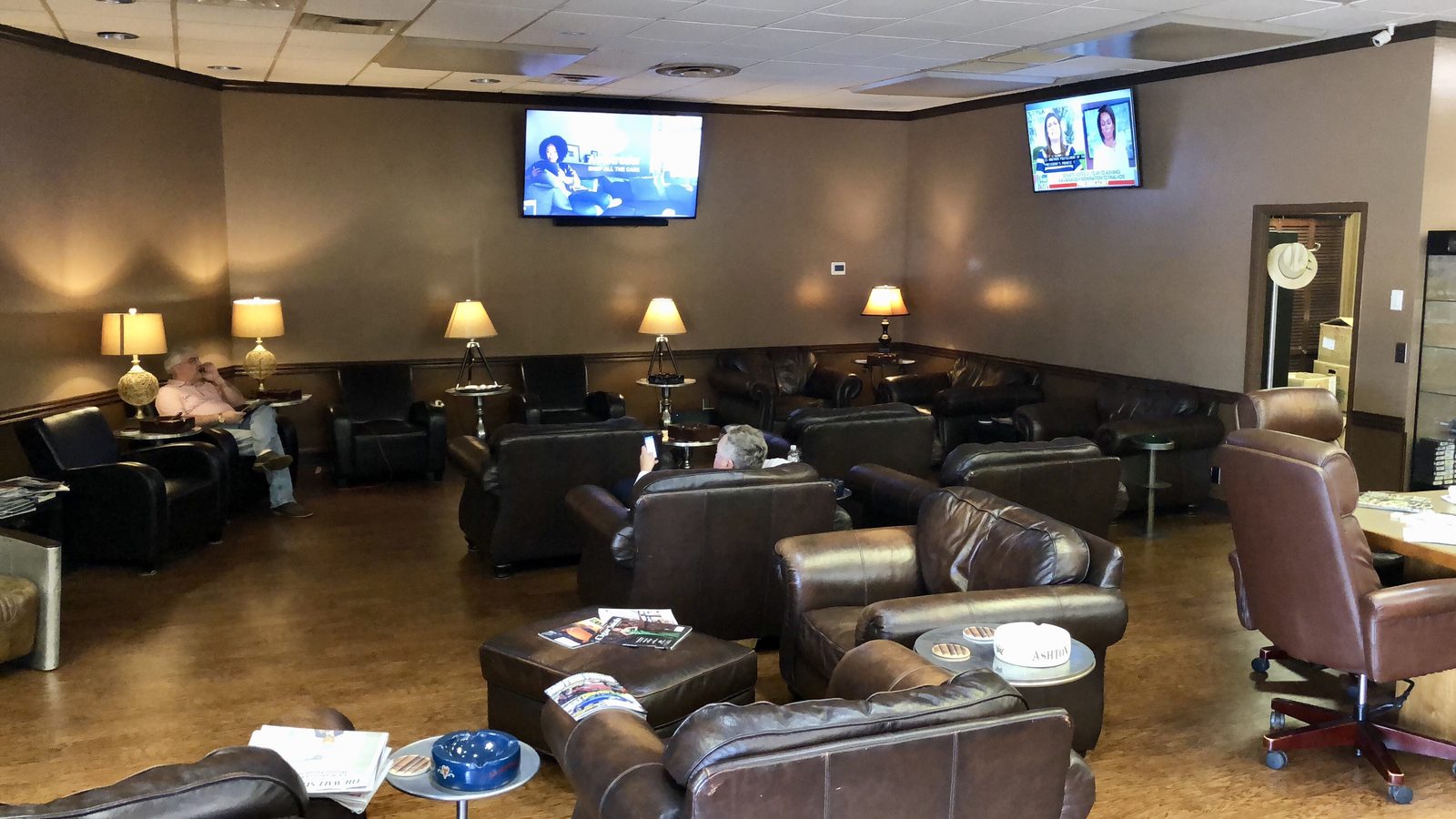 The Tobacco Pouch lounge with rows of leather armchairs, table lamps, and wall-mounted TVs